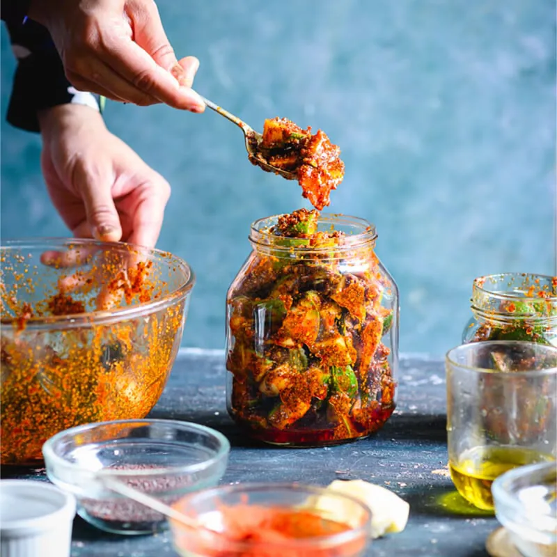 Hands spooning freshly mixed achar into a glass jar